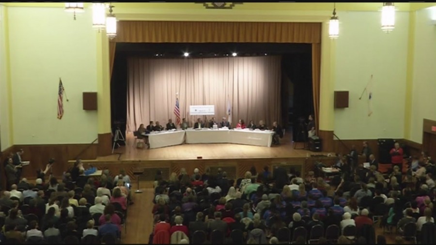 The Board of Education sits on stage, as a packed house from floor to balcony make their voices heard.